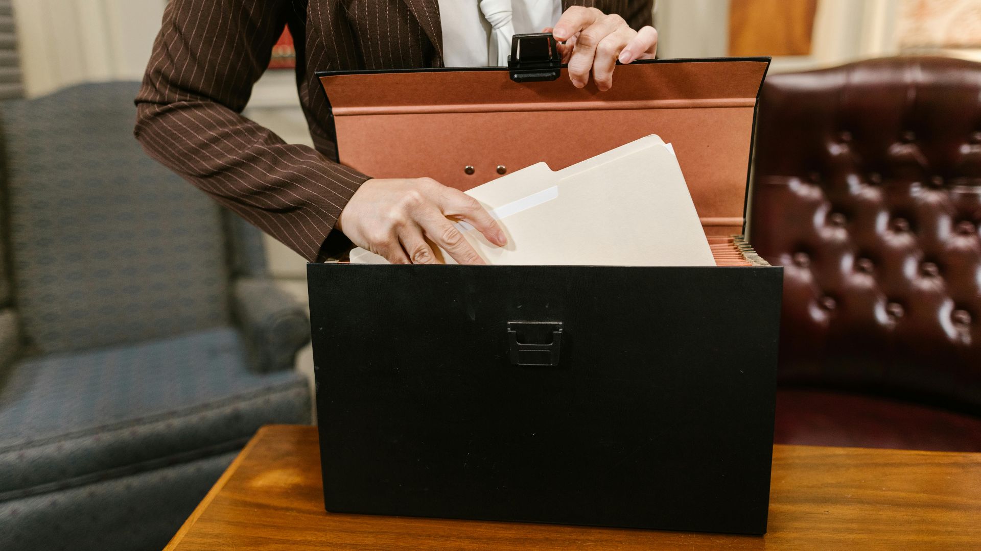 Close-up of a businesswoman organizing files in a black box in an office setting.