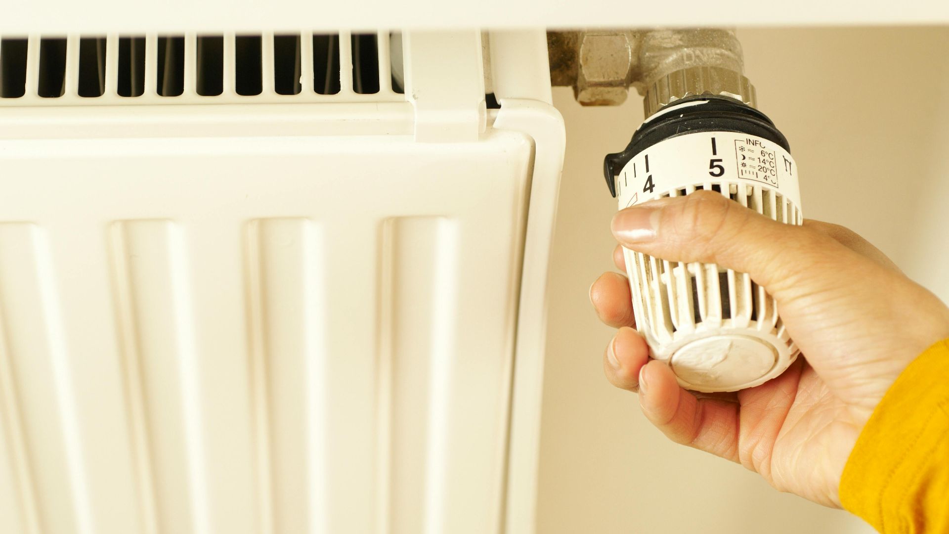 Close-up of hand adjusting radiator thermostat to control home heating temperature.