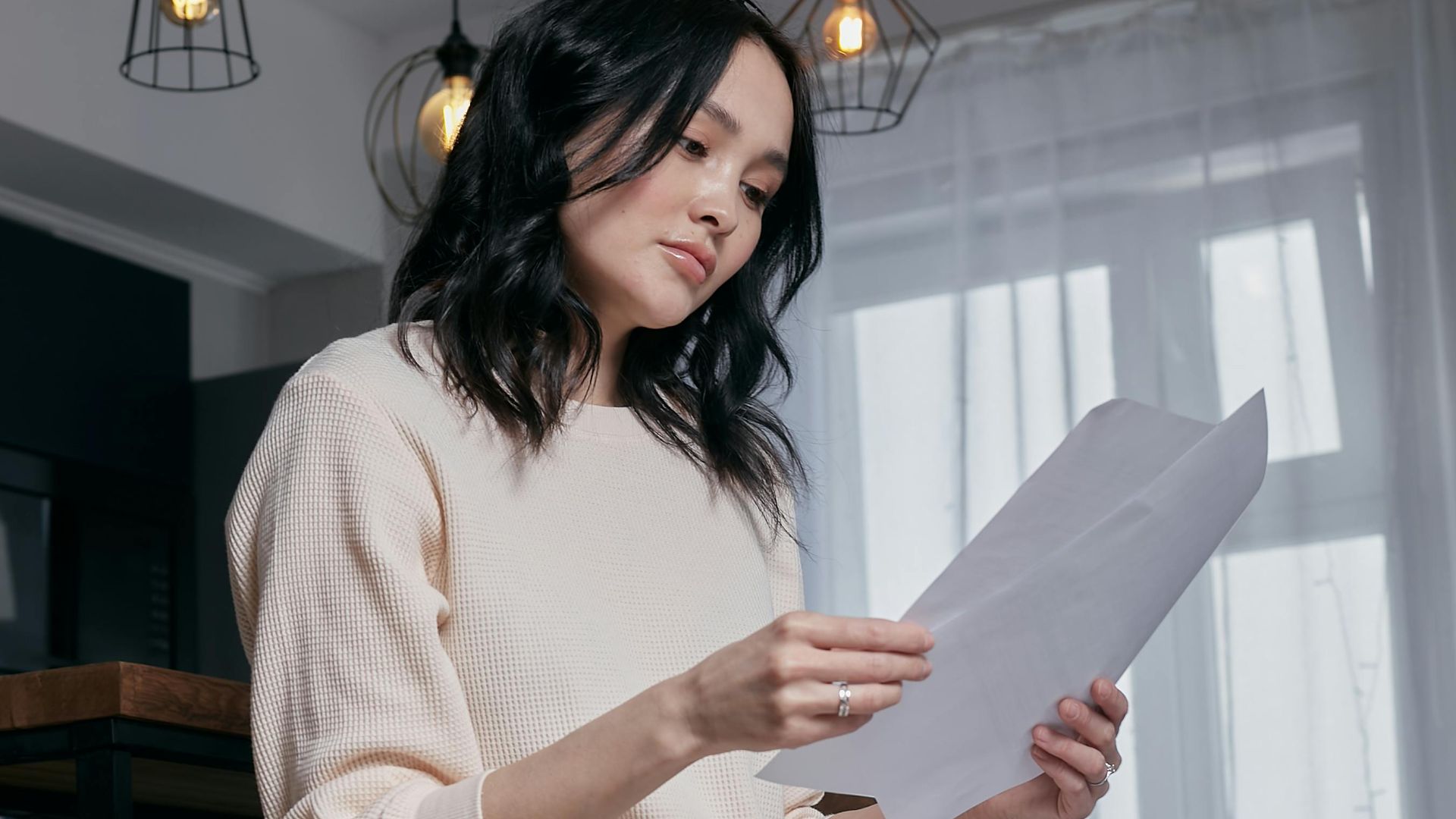 Casual woman reading documents in a stylish indoor setting with modern lighting.
