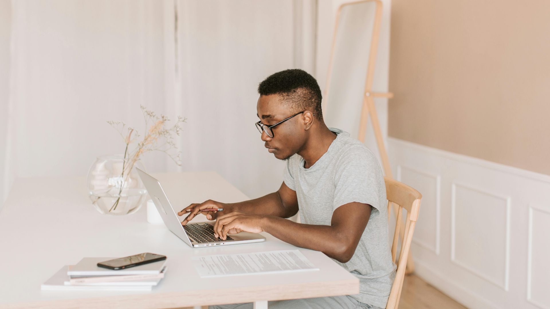 Adult man working from home, typing on laptop in a bright, modern home office setting.