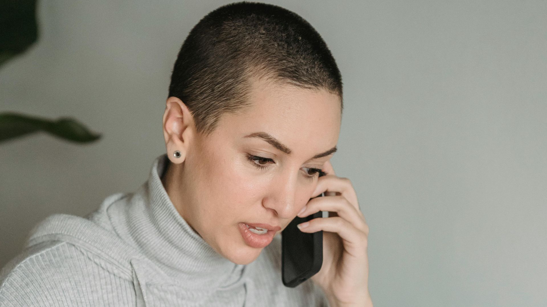 Concentrated young female in gray domestic clothes browsing netbook and having conversation via cellphone in light room