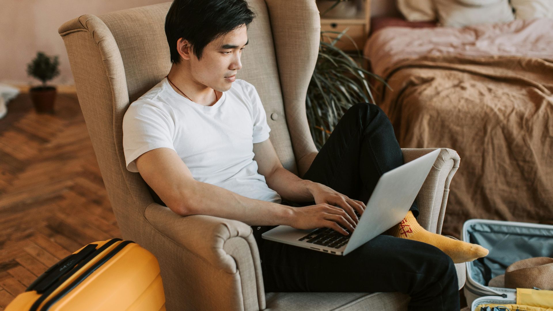 A man sitting comfortably in an armchair, using a laptop in a cozy home interior.