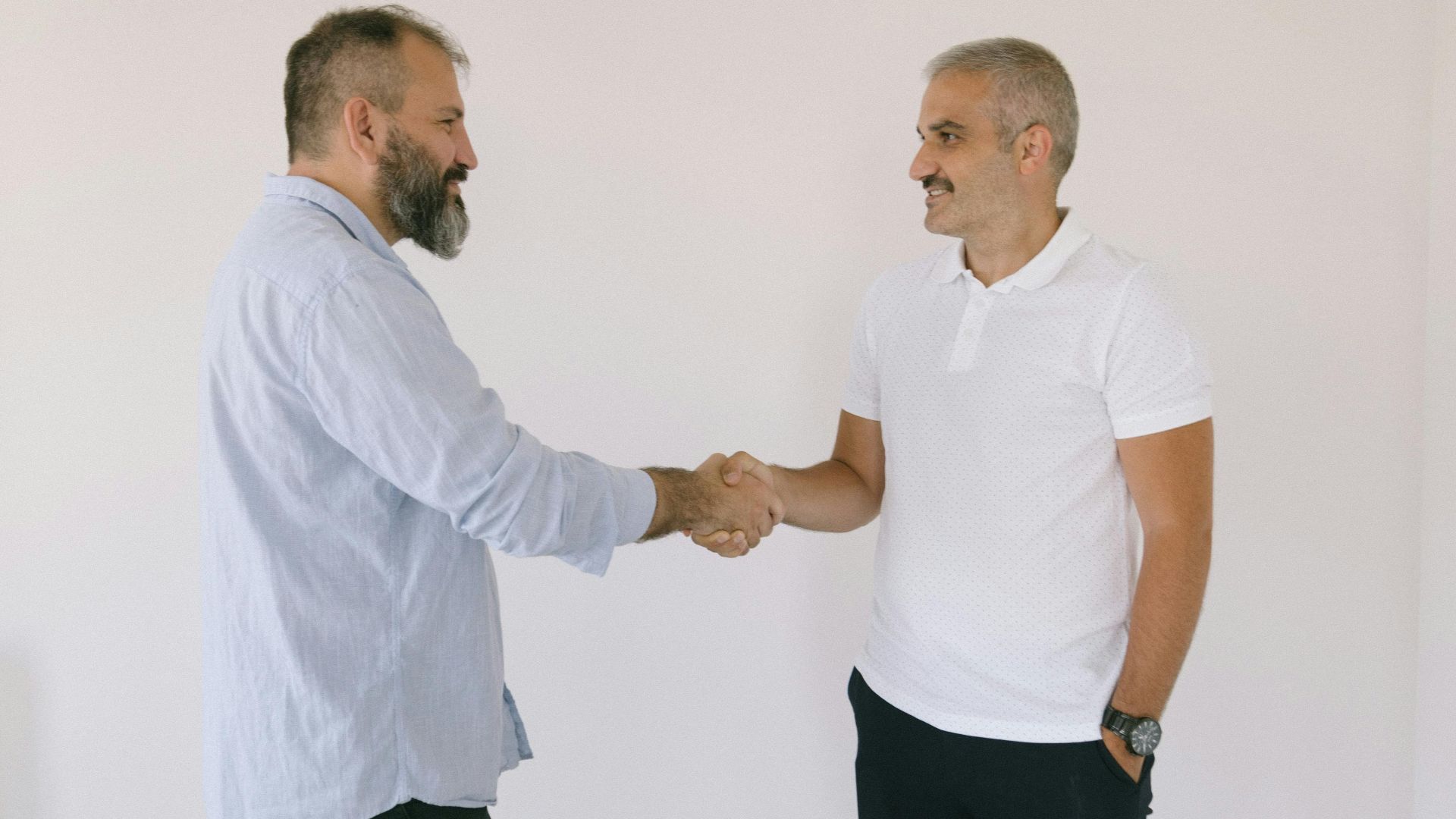 Two men exchange a handshake indoors, symbolizing agreement or partnership.