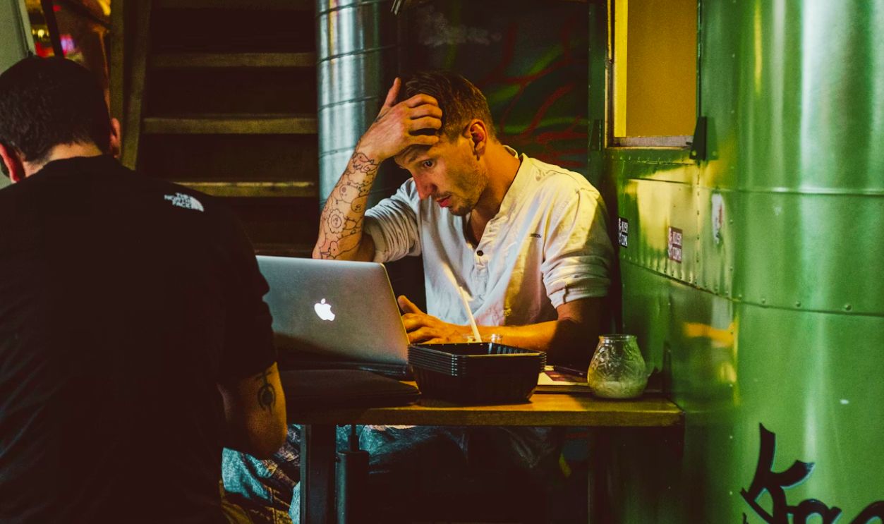 man in front of silver MacBook while scratching his head