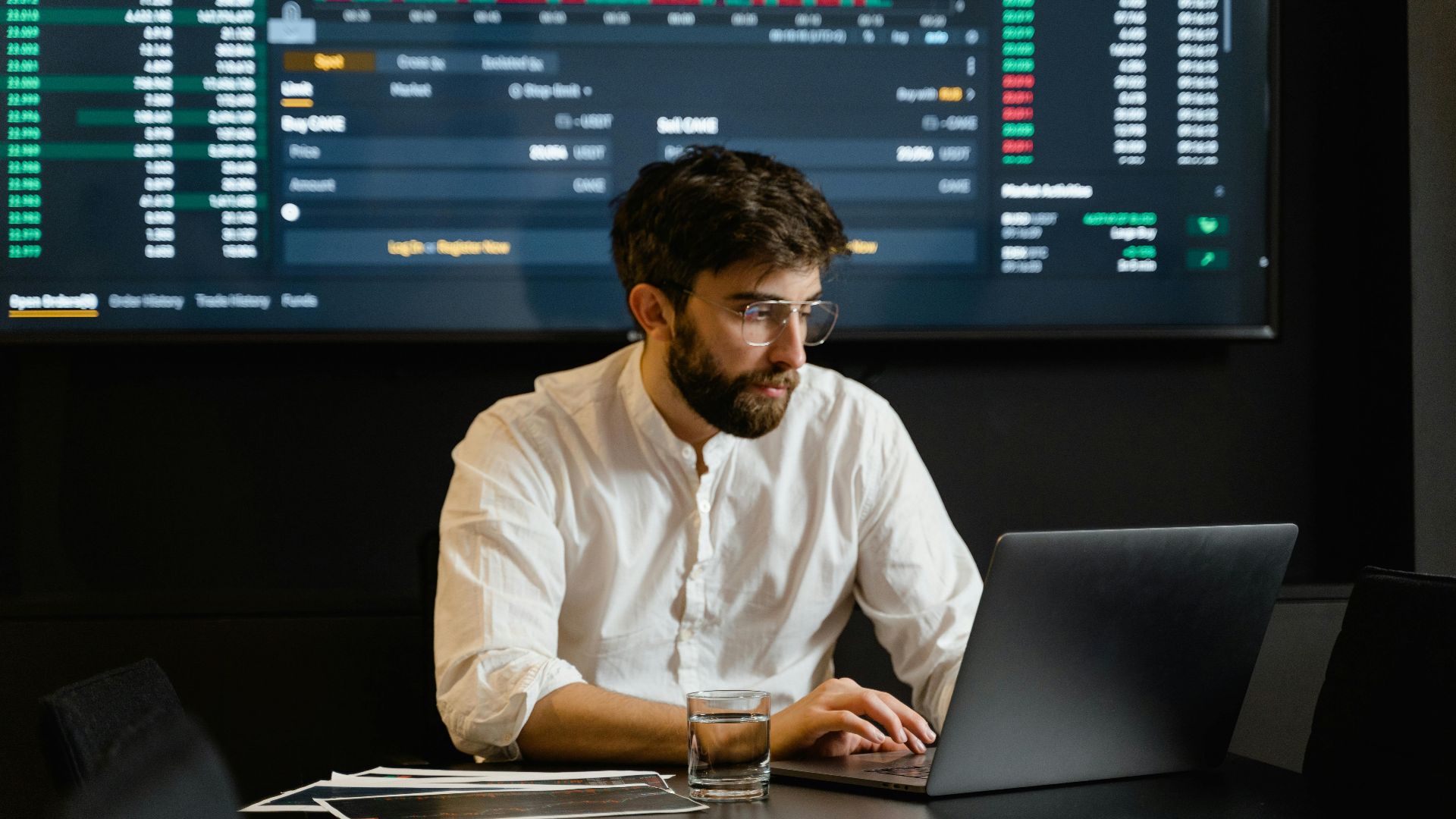 Professional analyzing stock market trends using laptop and digital display in modern office.