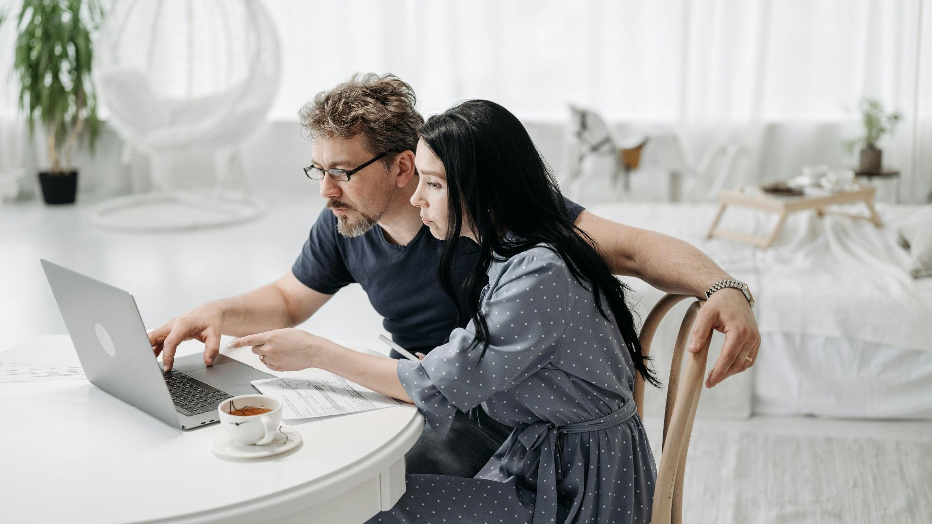 A man and woman sitting indoors, collaborating on a laptop at a table with coffee.