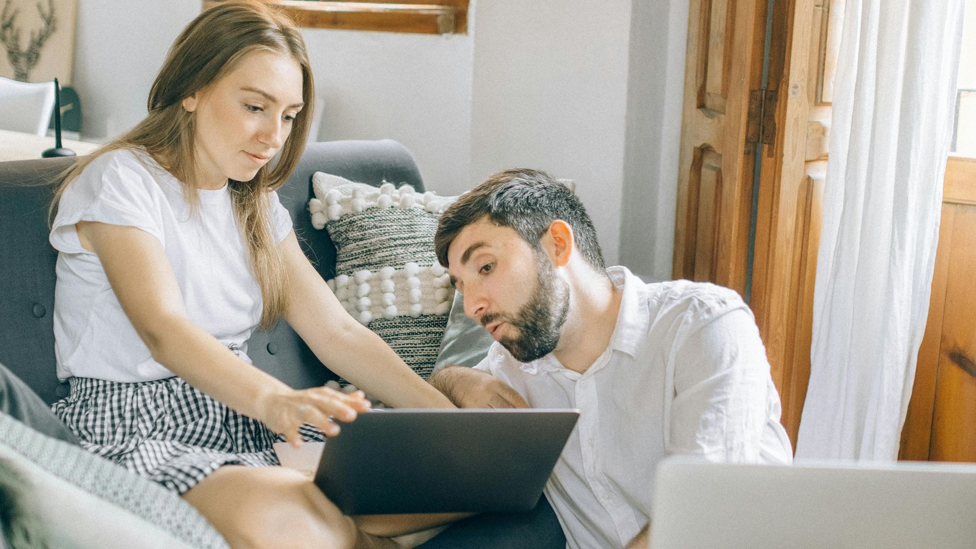 A young couple working together on laptops in a cozy living room setting, representing remote work.
