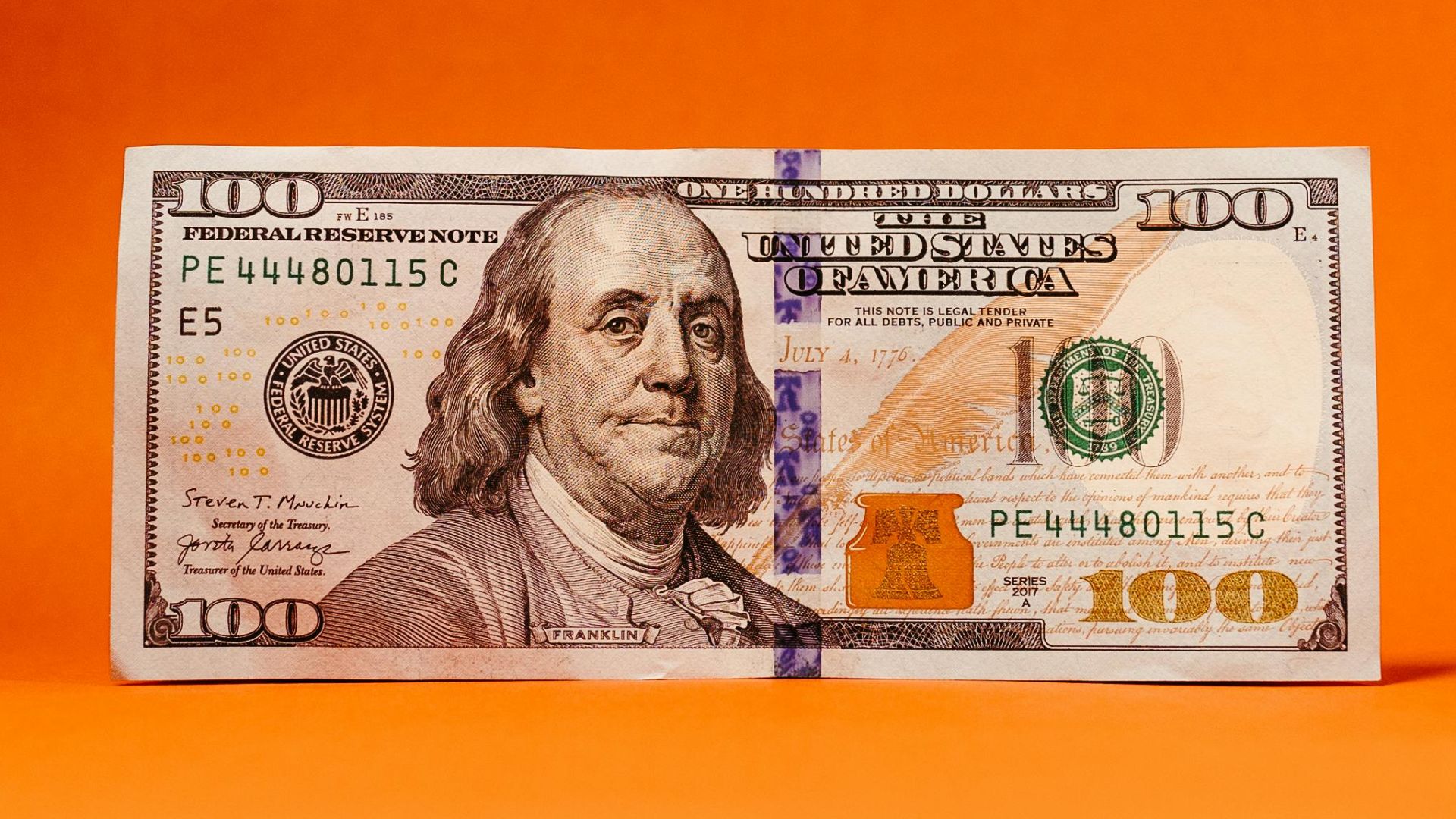 Crisp US hundred-dollar bill against a vivid orange backdrop. Ideal for finance themes.