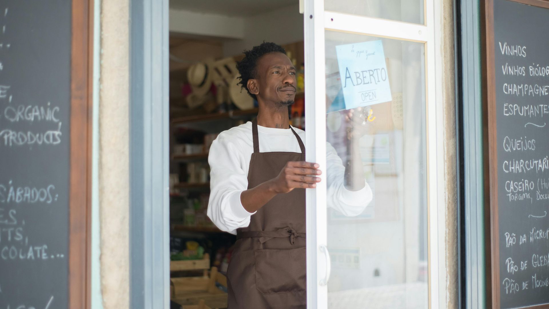 A man in an apron opens a grocery store door in Portugal, ready for business.