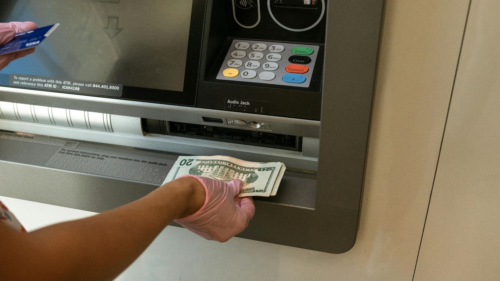 A person wearing gloves withdrawing cash from an ATM machine showcasing money handling and hygiene.