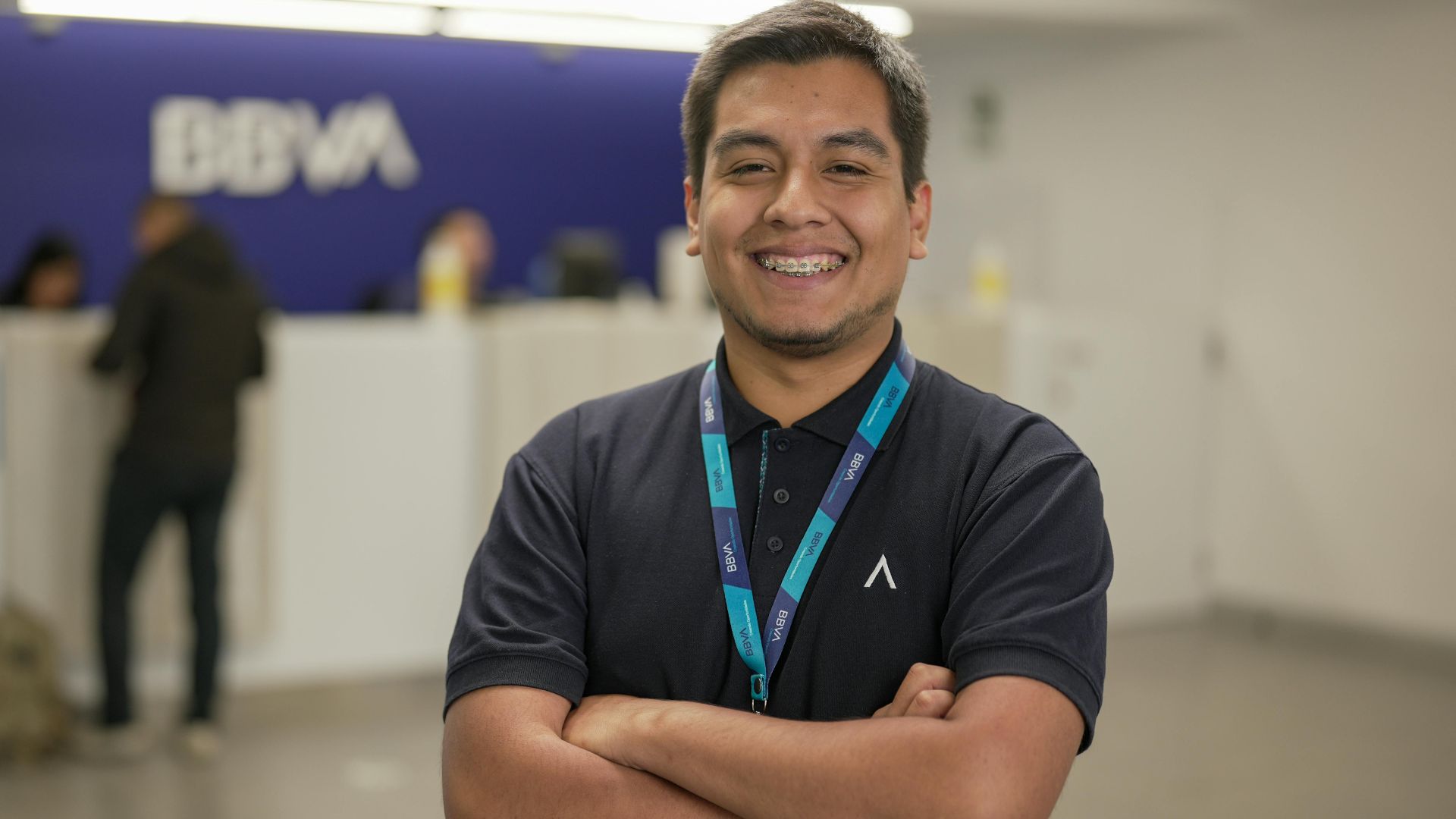 Confident bank employee standing with arms crossed at BBVA reception area, smiling warmly.