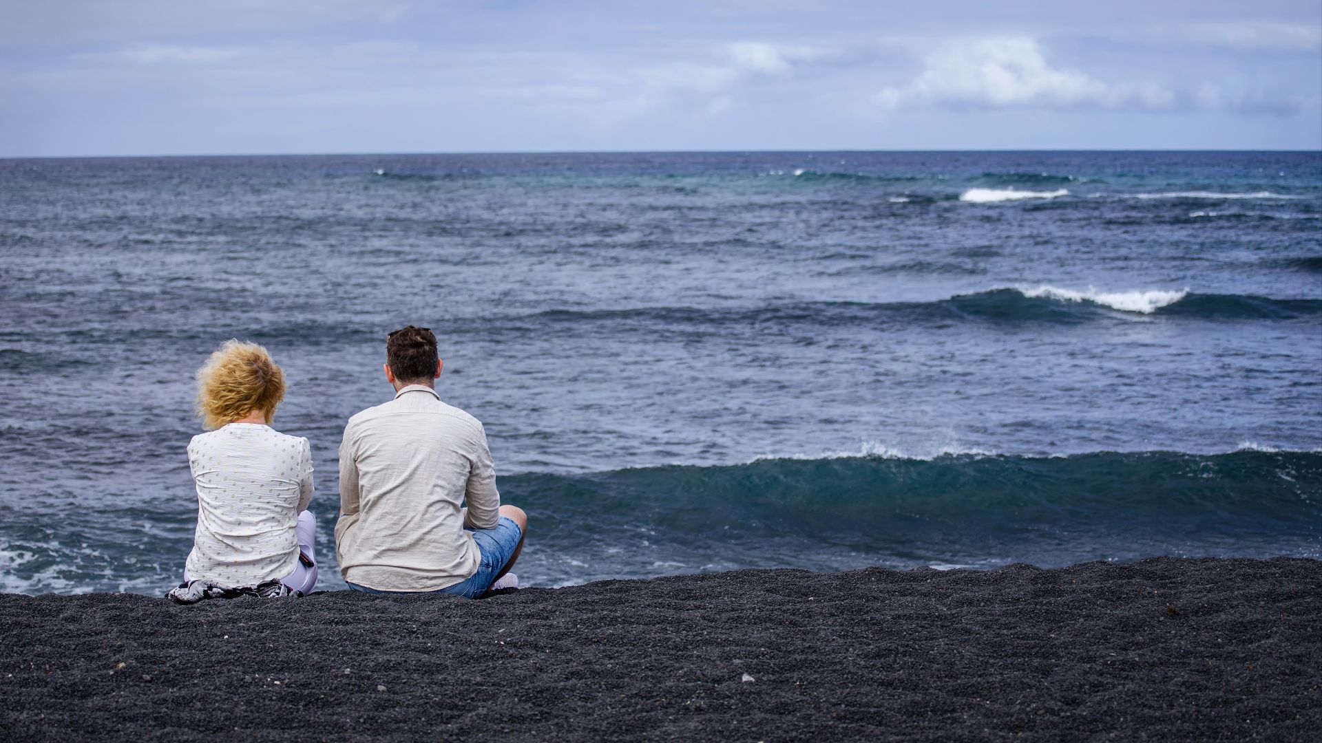 Couple sitting on a black sand beach watching waves