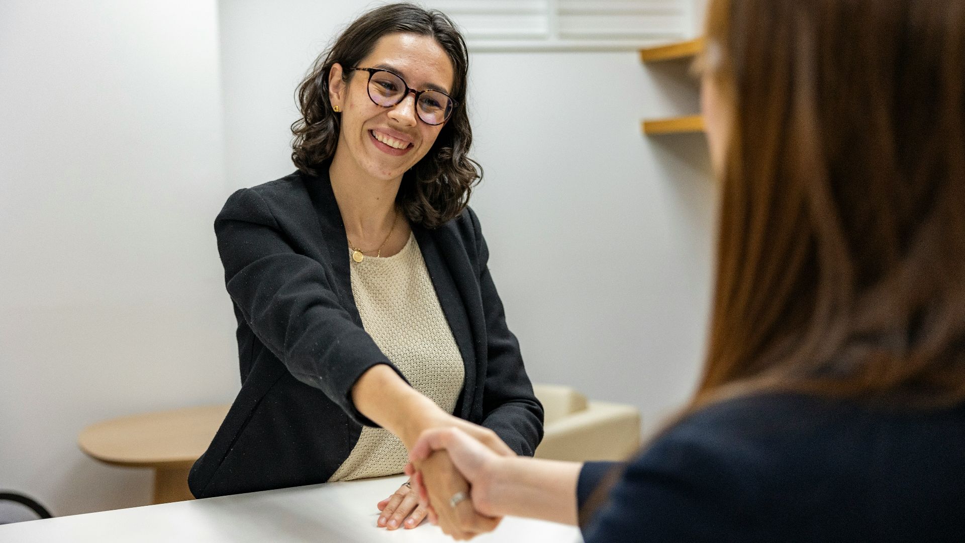 a woman shaking hands with another woman sitting at a table