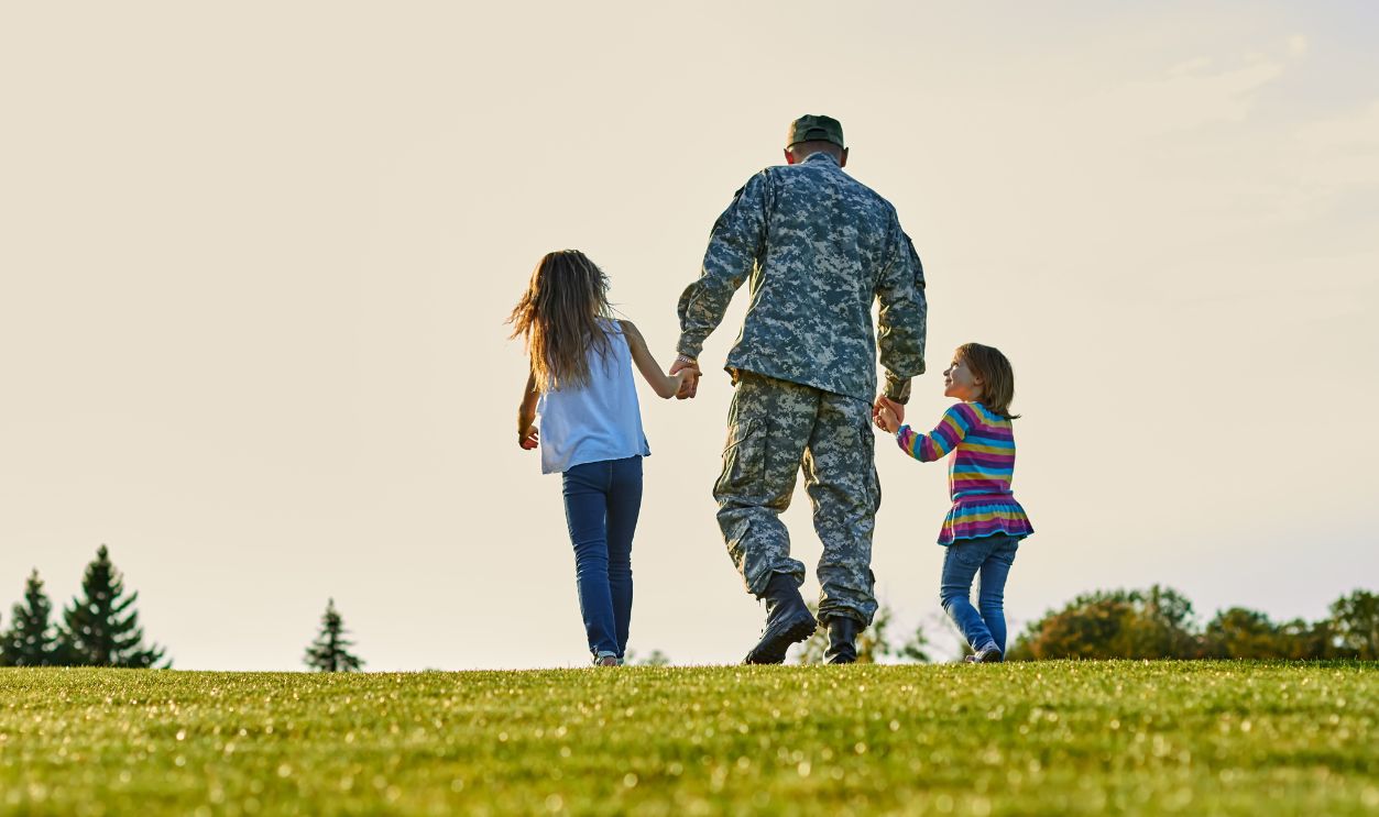 Soldier walking with little girls holding hands. Back view, father and daughters are walking together.