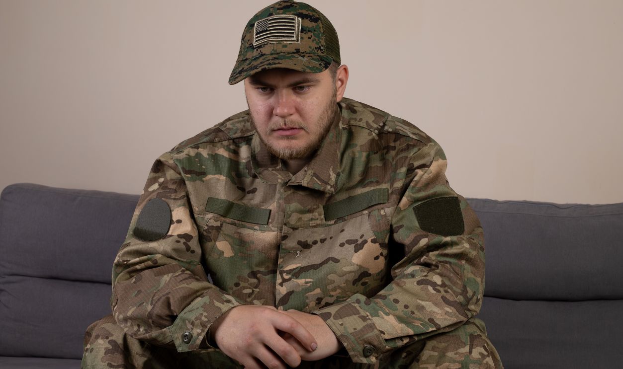 The soldier is sitting on a couch, possibly resting or waiting for orders