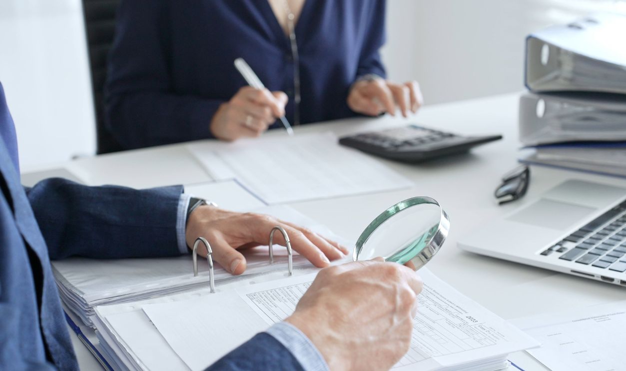 Two professional chartered accountants reviewing financial reports and analyzing data using a calculator and a magnifying glass, ensuring accuracy and compliance. Audit and taxes in business