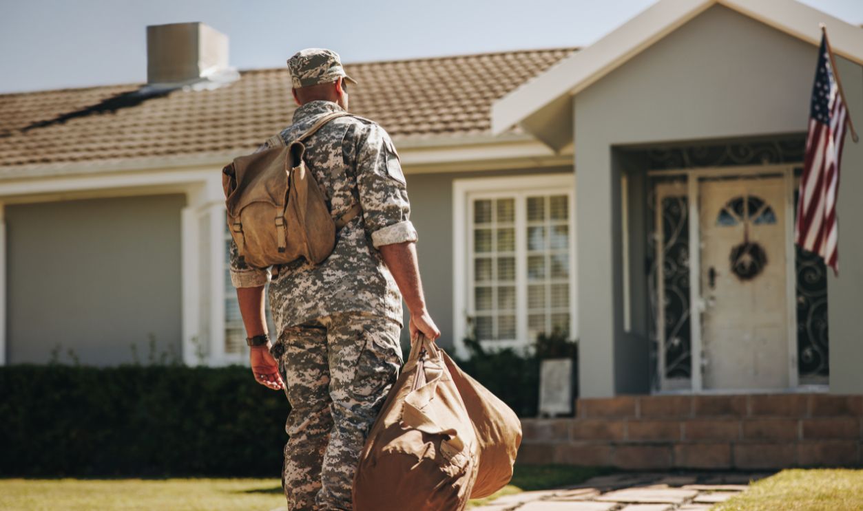 Patriotic young soldier walking towards his house with his luggage. Rearview of an American serviceman coming back home after serving in the military.