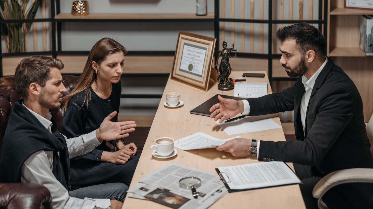 Young couple are seating and talking with lawyer at his office.