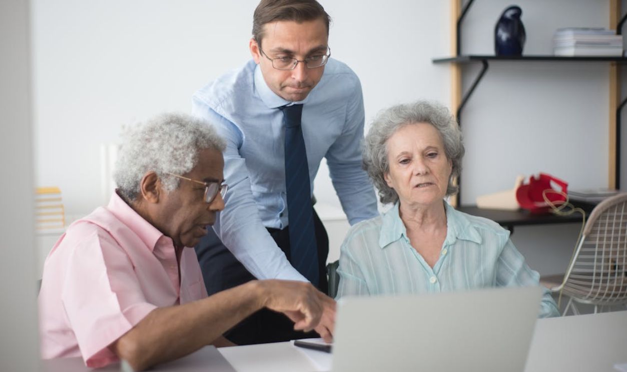 A Man Standing Between Elderly People Sitting at a Desk