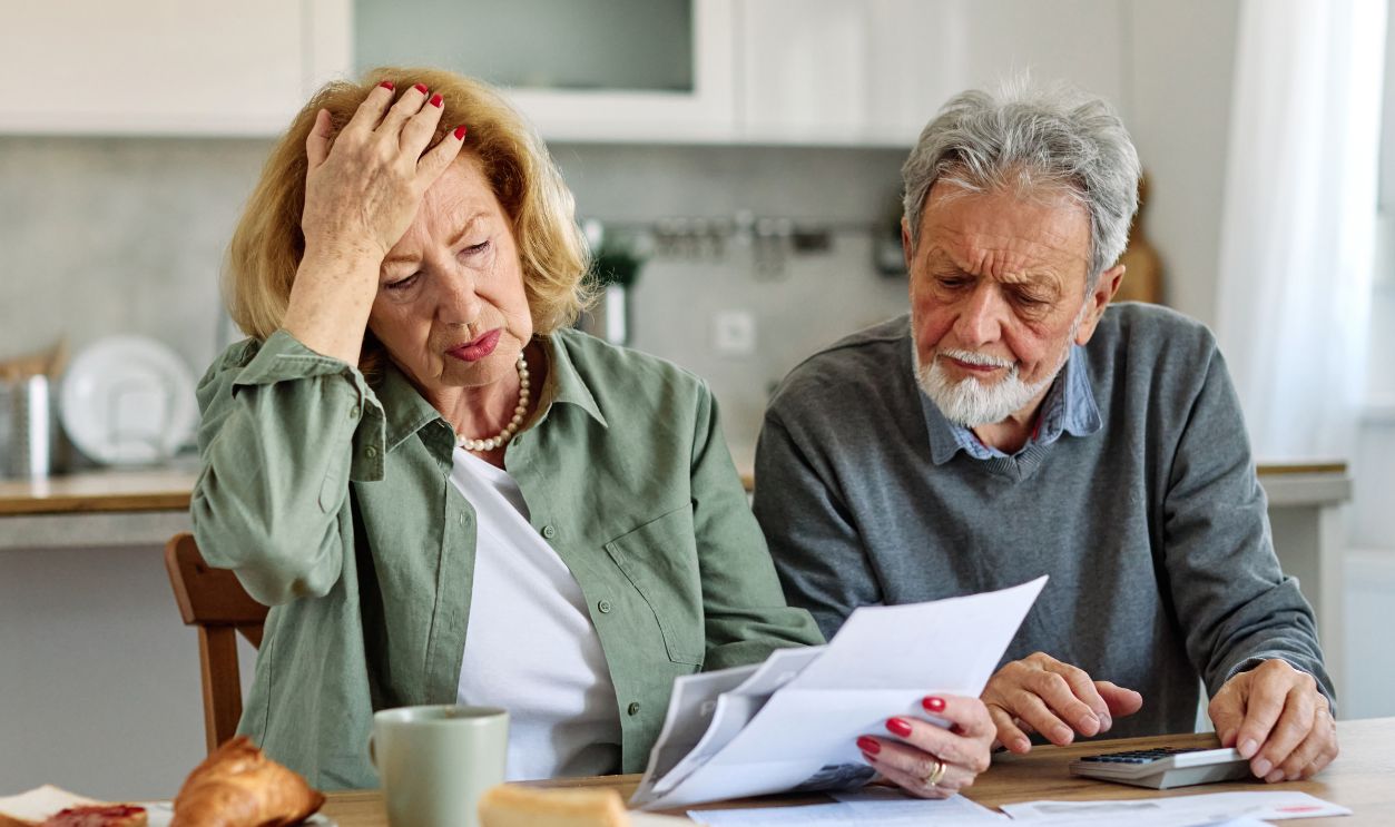 Senior couple checking bills and calculating expenses using a calculator at home, debt taxes and home budget concept, worried married elderly couple