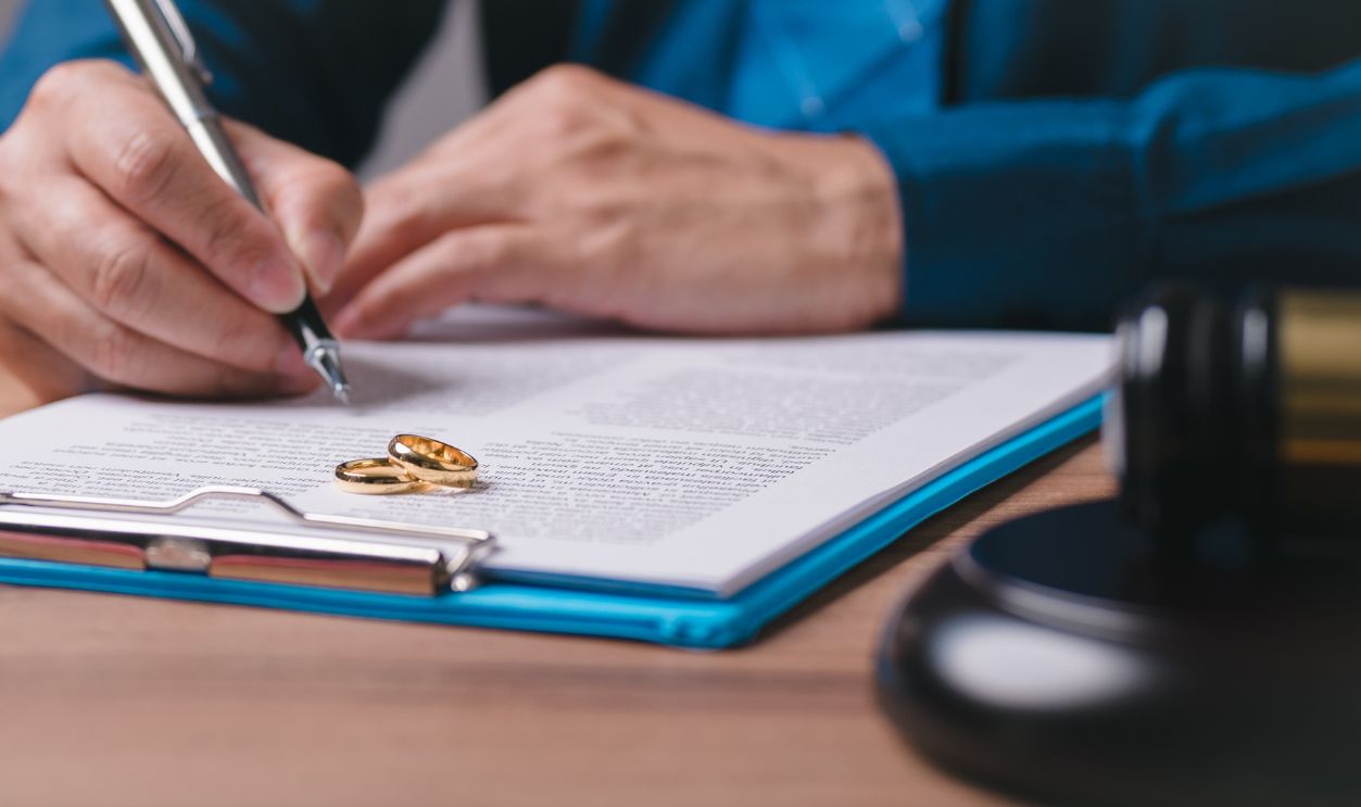 A man is writing on a piece of paper with a pen. The paper has a ring on it