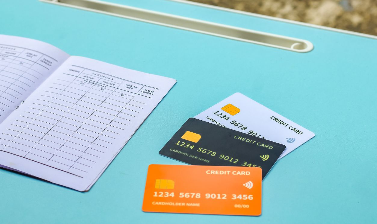 close up of an open bank passbook with blank transaction fields, accompanied by three orange,black and white credit cards isolated on a blue background