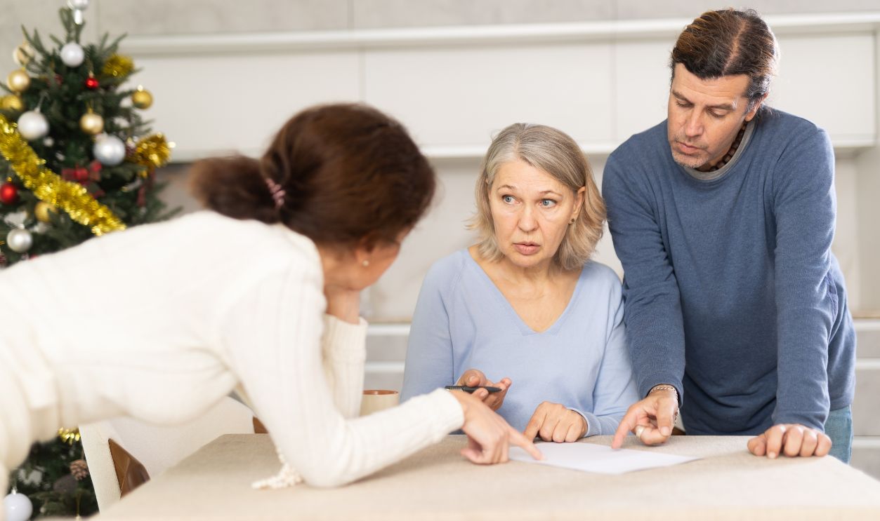 Adult children help an elderly mother and tell her how to make a will while sitting at home in the kitchen during Christmas.