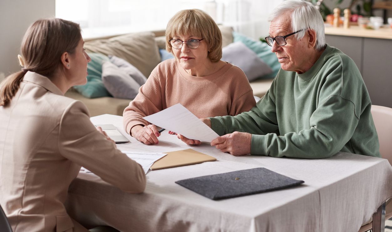 Senior couple sitting at the table with financial advisor reading documents and consulting in the room