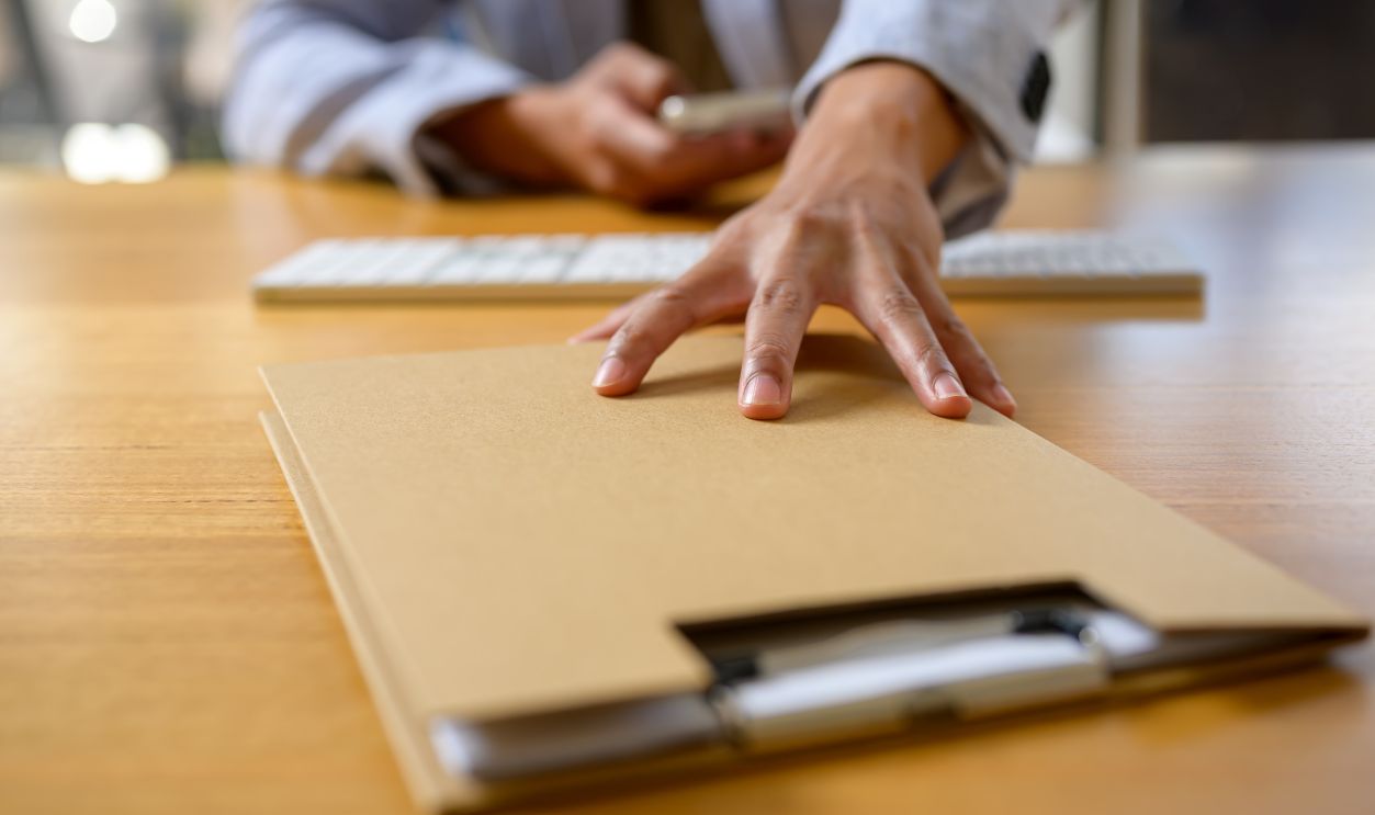 Close-up of a businessperson's hand reaching for a confidential folder on an office desk, symbolizing urgency, data handling, document management, and business communication in the workplace