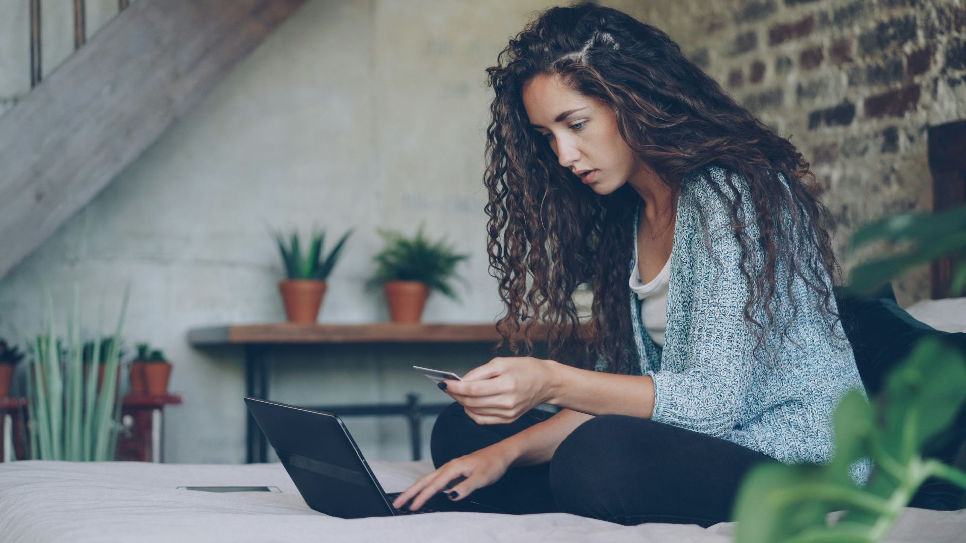 Woman using laptop and credit card on bed.