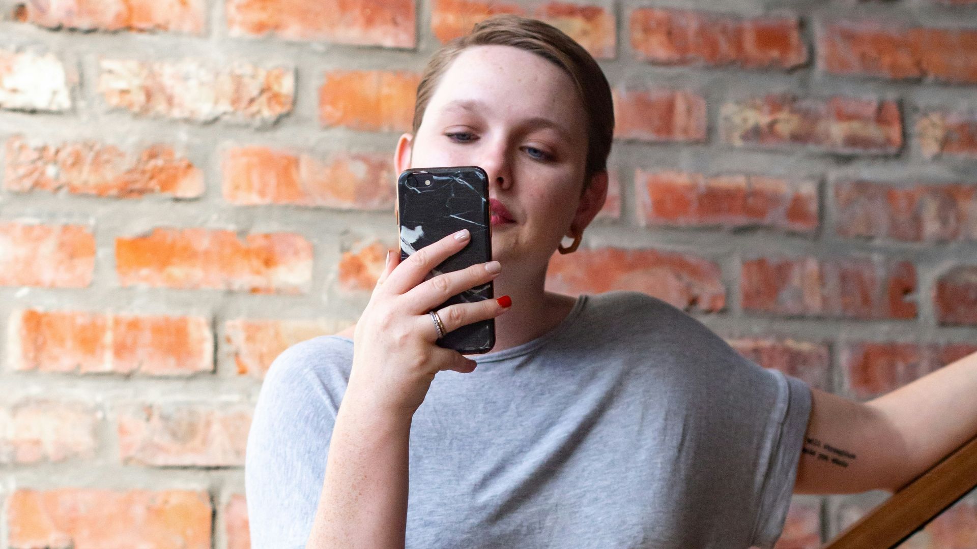 woman in gray crew neck t-shirt and black skirt holding black smartphone