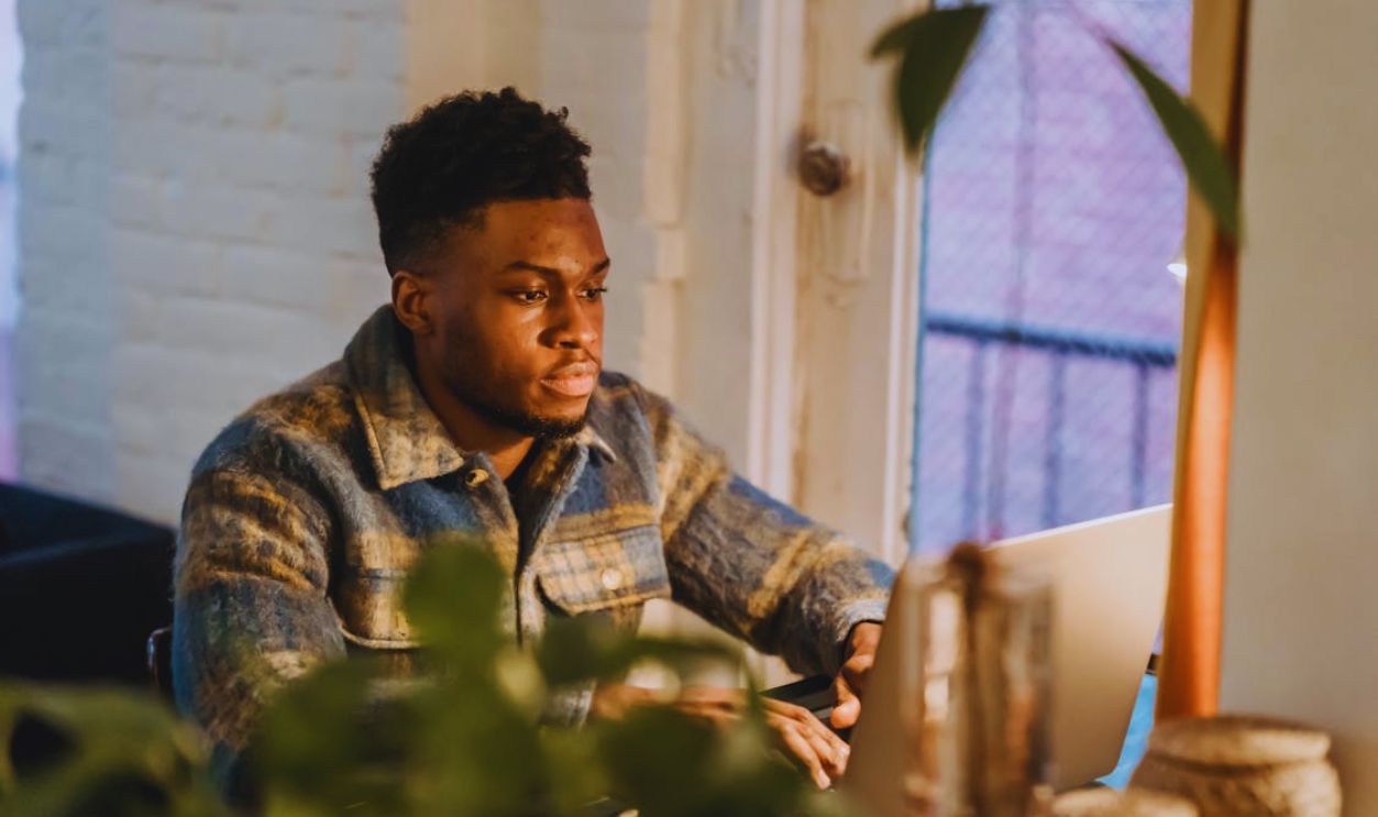 Black bearded man typing on laptop at home