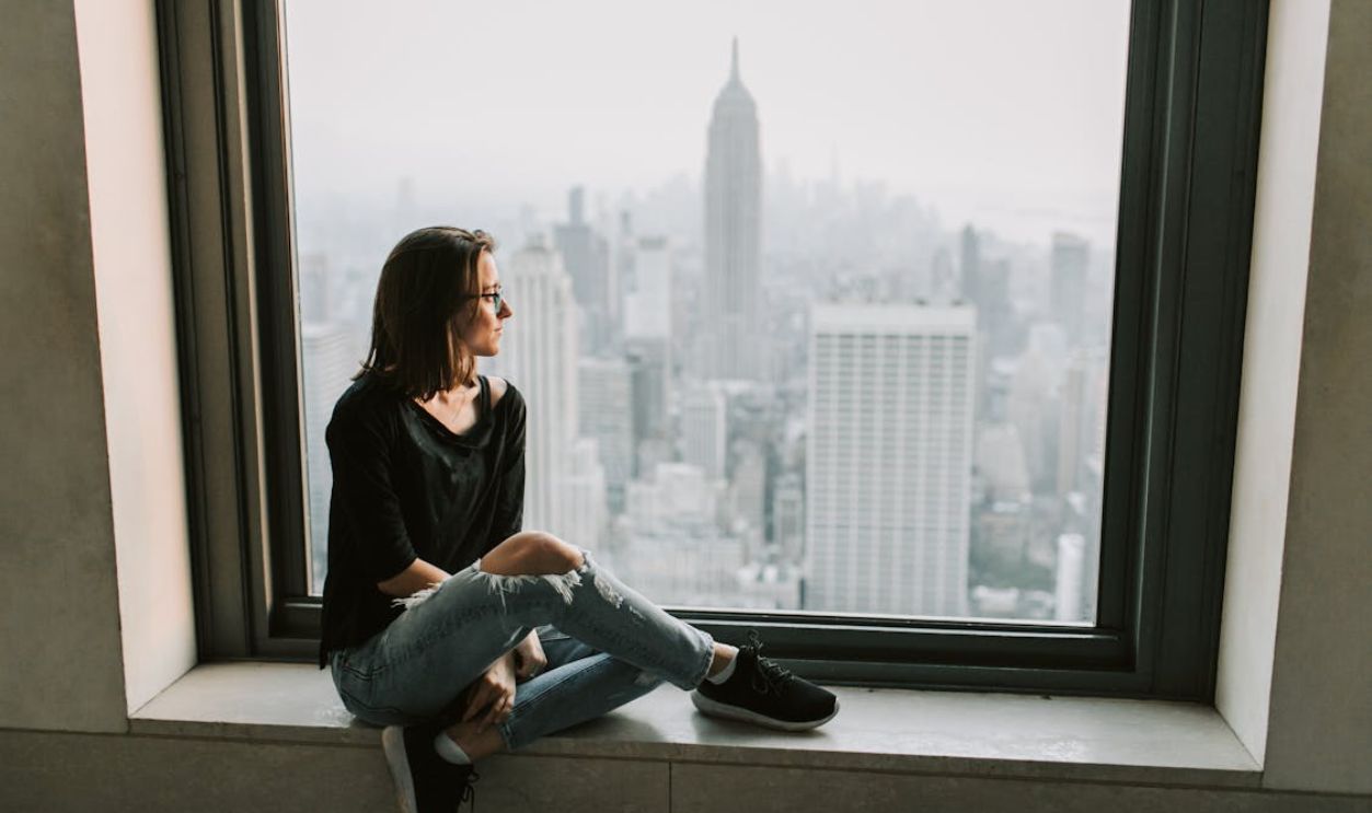 Woman in Black Jacket and Blue Denim Jeans Sitting on Window with the View on Empire State Building