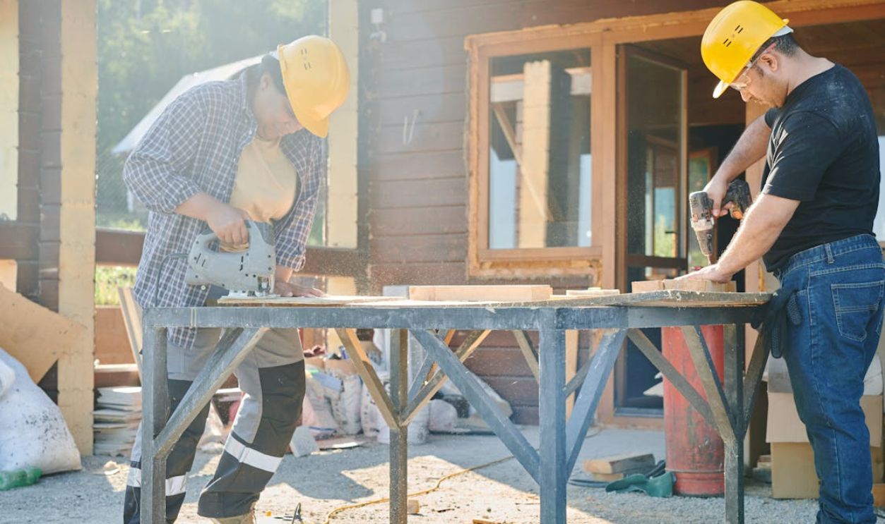 Man and Woman in Yellow Hard Hats Working Using Industrial Tools