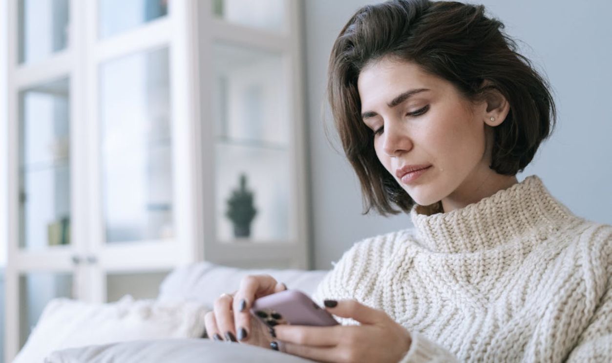 A Woman in White Knitted Sweater Using a Cellphone