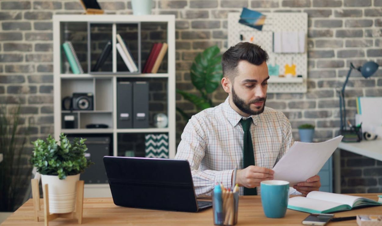 Man in Shirt Sitting at Office and Reading Document