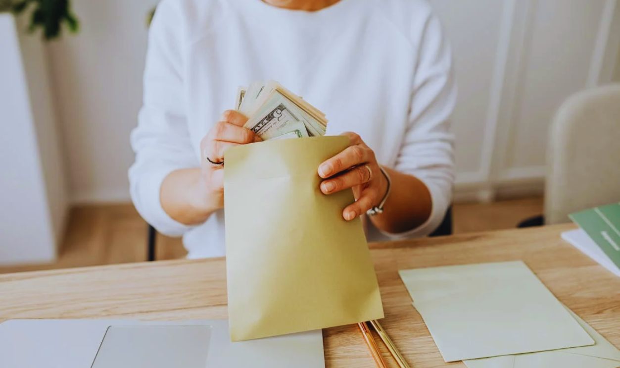 Person Wearing a Sweater Putting Money Inside an Envelope