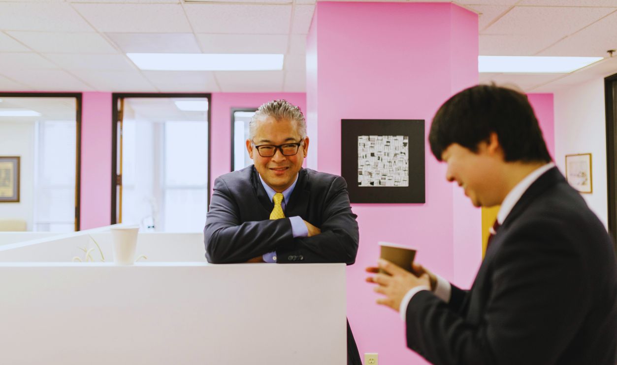 Man in Black Suit Leaning with Arms on White Panel