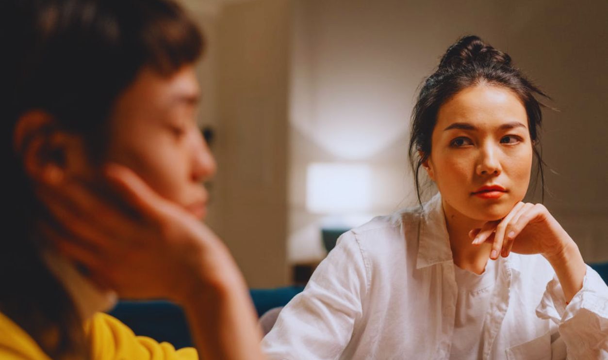 Thoughtful young ethnic women having conversation at table at home