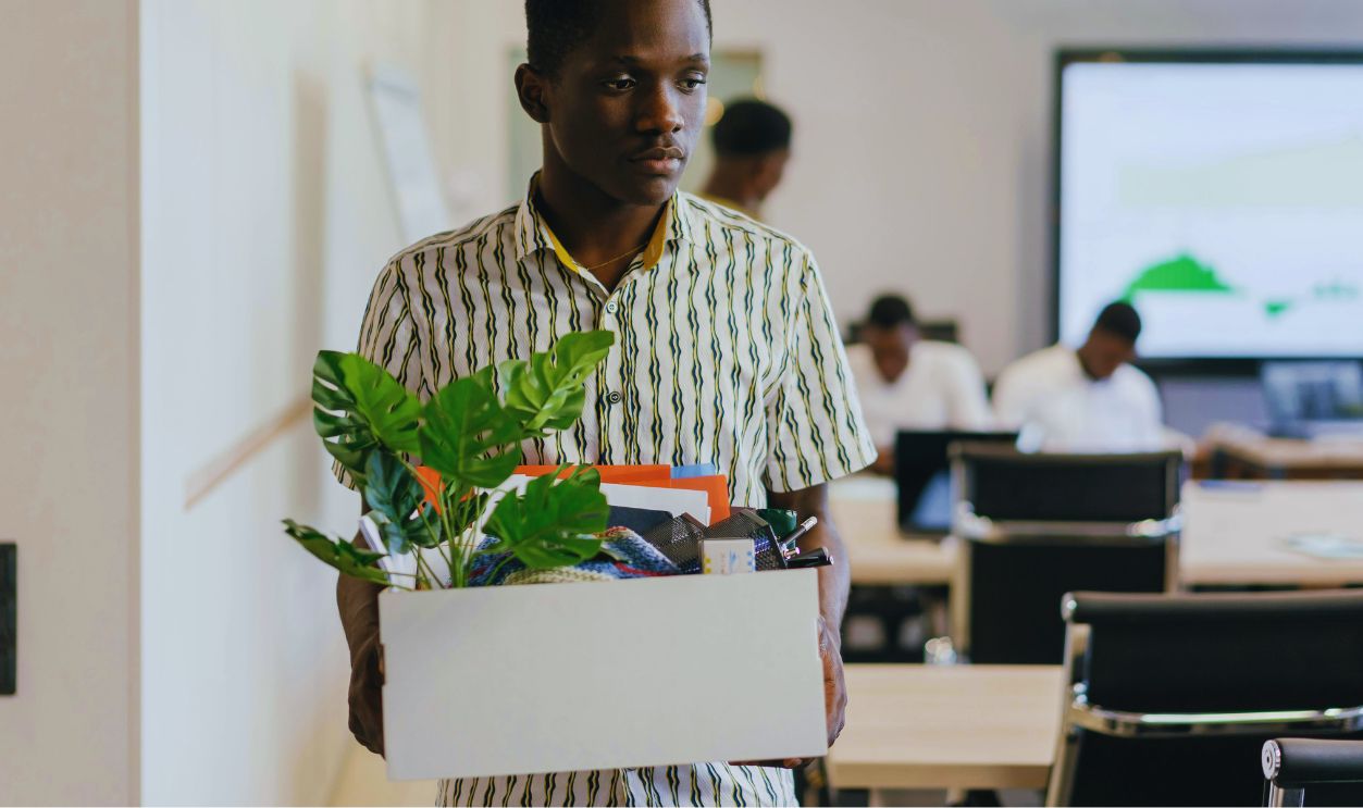 Sad Man in Button Down Polo Carrying White Box with Green Plant and Things in it