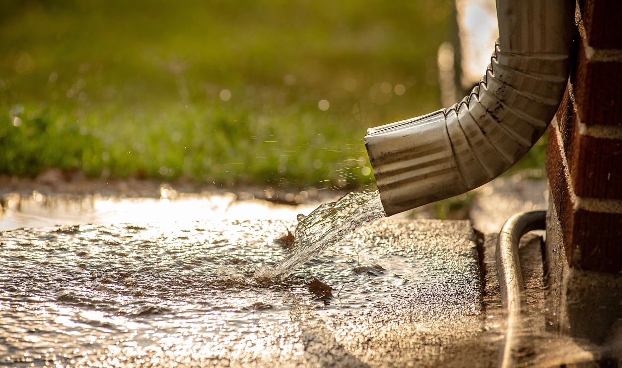 Closeup of residential home gutter downspout gushing out water during rain storm in suburbs. 