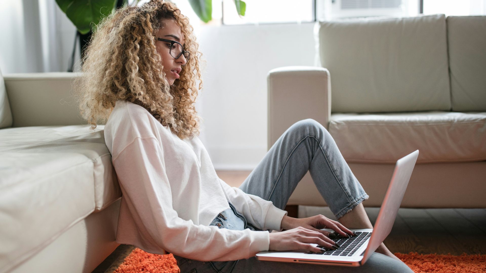 woman sitting on floor and leaning on couch using laptop