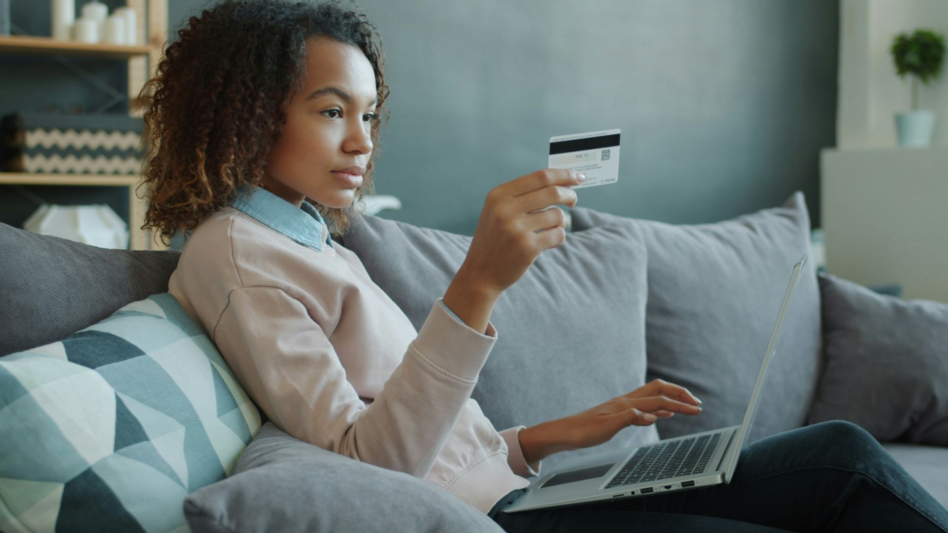 Woman using laptop and credit card on sofa