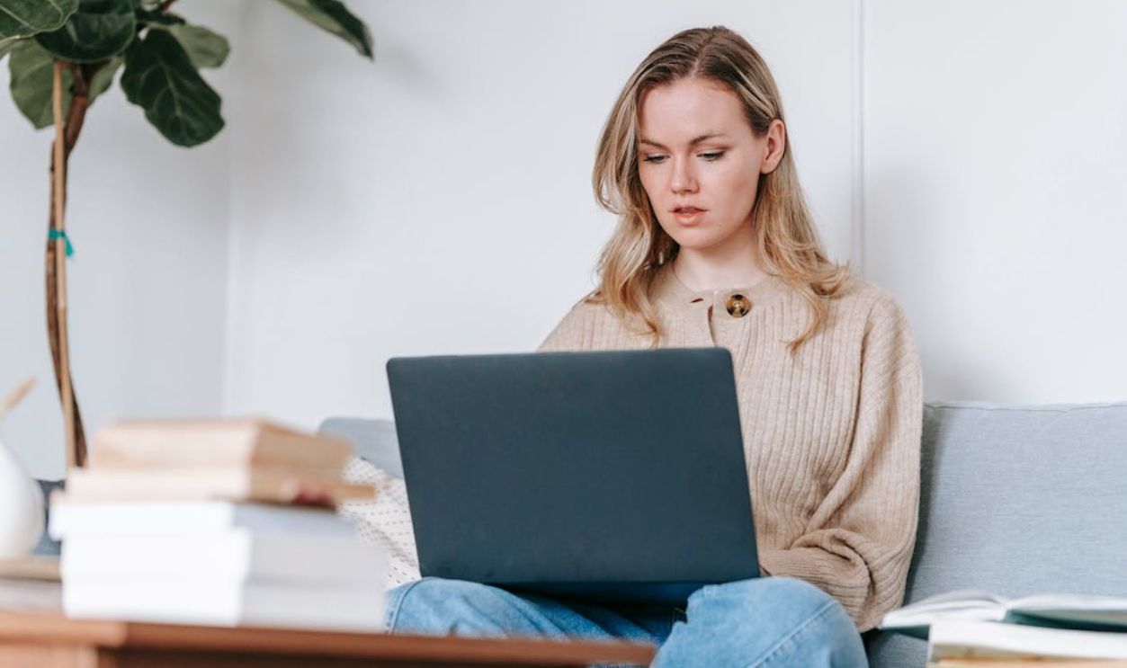 Attentive student with laptop studying on sofa at home