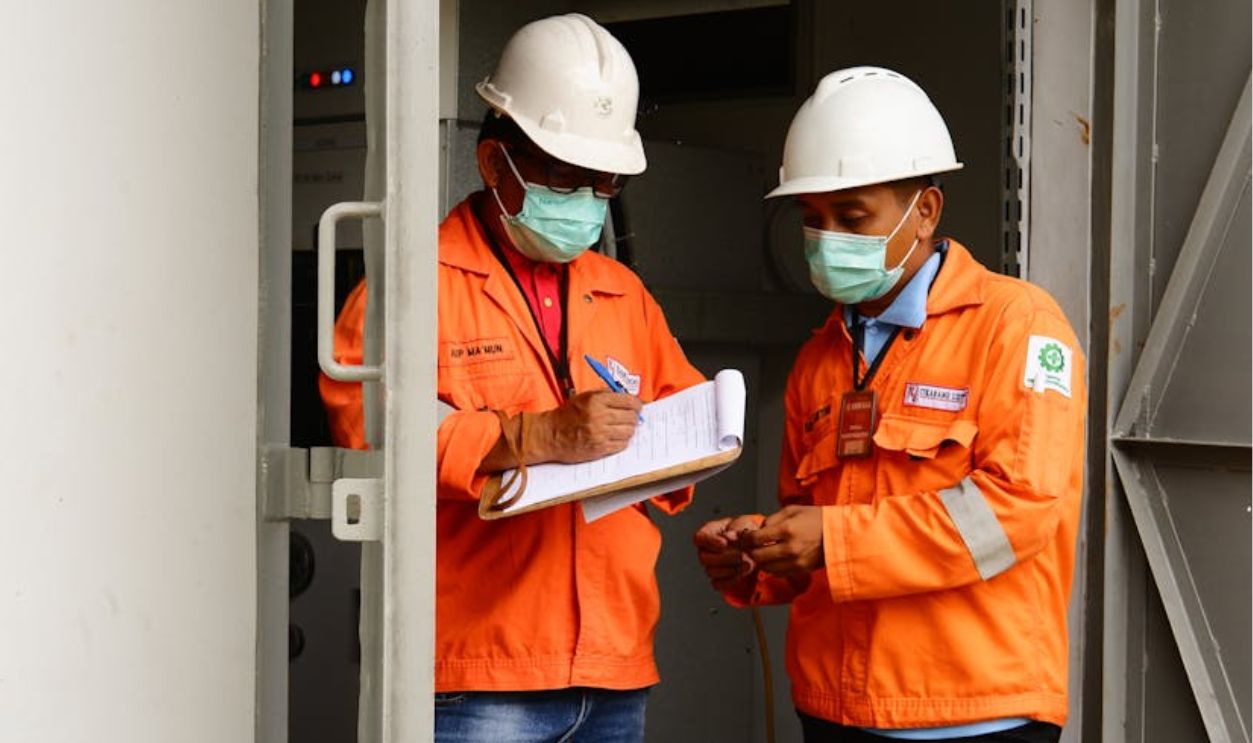 Men in Orange Jacket and Hardhat Standing on the Doorway