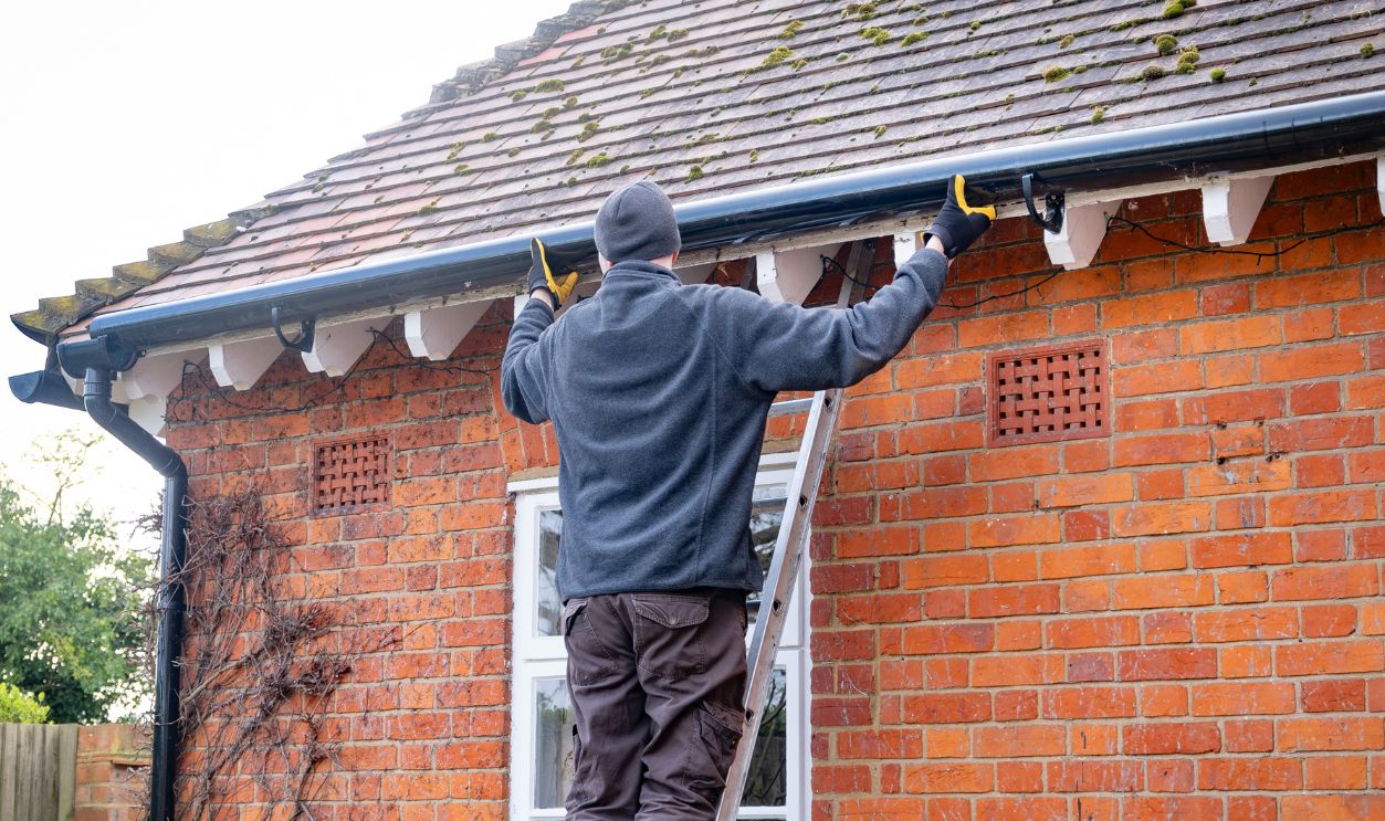 Man on a ladder fixing fitting a rain gutter on the eaves of a UK house