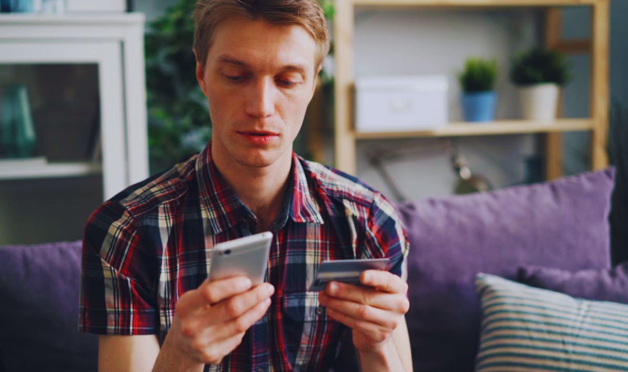 Man Sitting on a Sofa Holding a Smartphone and a Credit Card in his hands