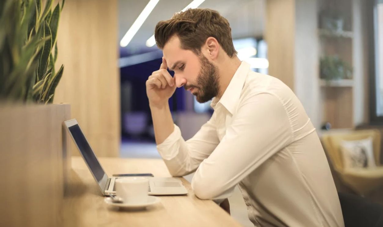 Man With Hand on Temple Looking at Laptop