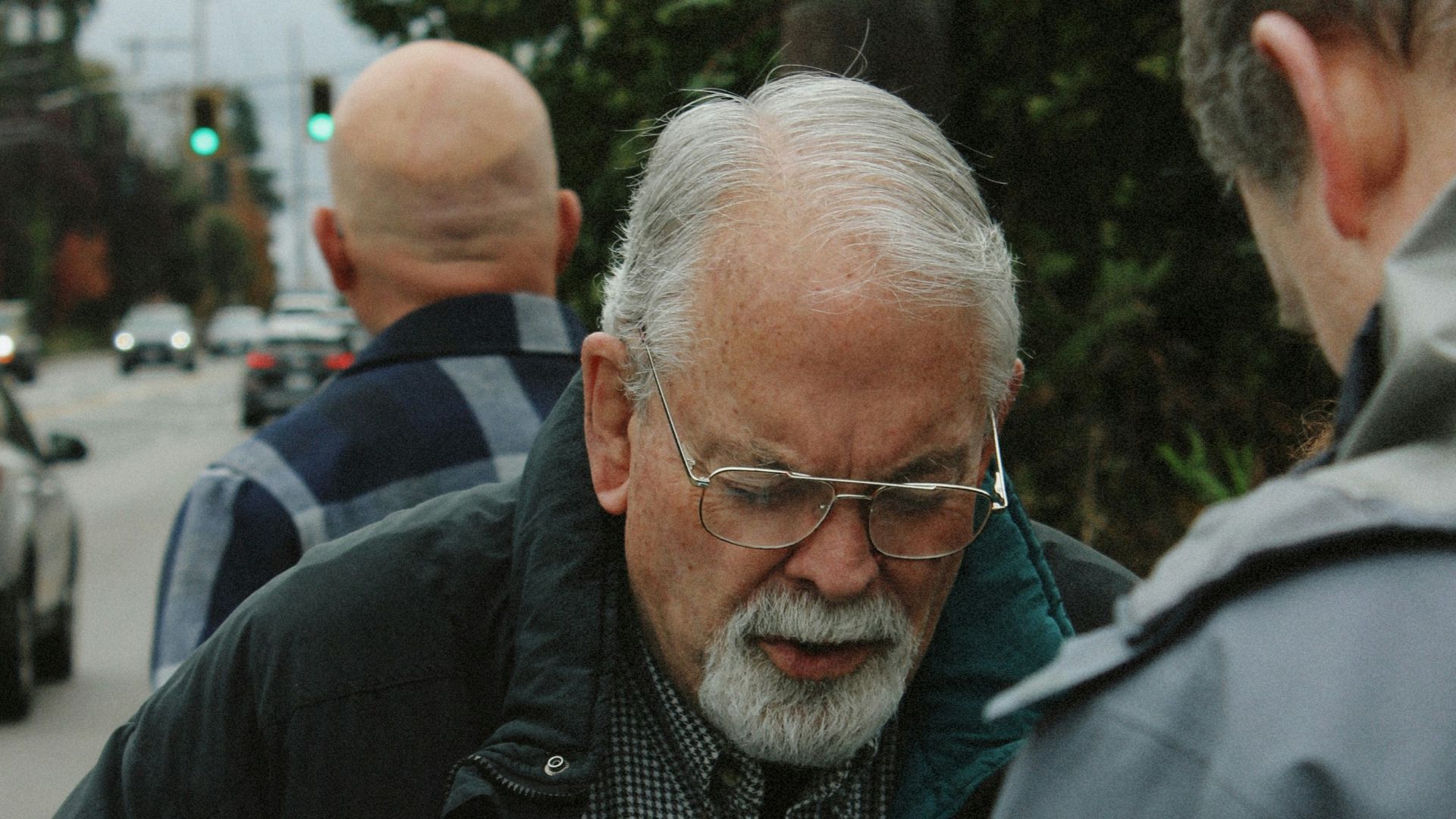 Elderly man holding a pamphlet with glasses and beard.