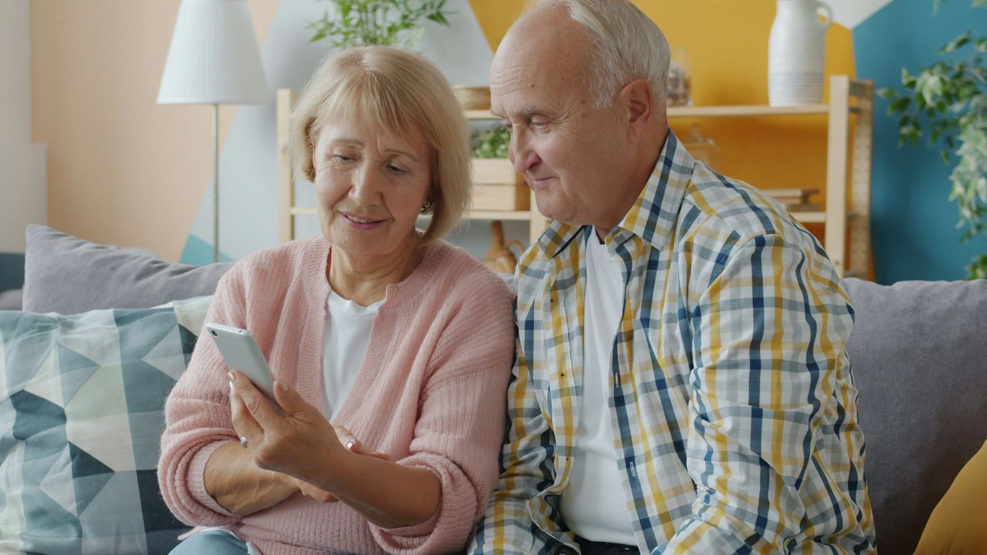 Elderly couple looking at a smartphone together on couch.
